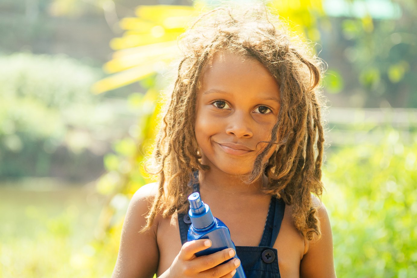 Mowgli indian boy with dreadlocks hair hiding holding mosquito spray in tropics green forest background